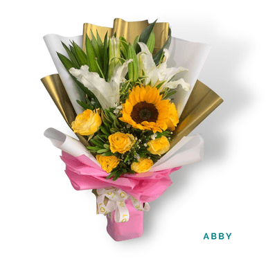 Abby arrangement on a plain background: Vibrant sunflowers, lilies, and yellow roses with elegant gold and pink accents