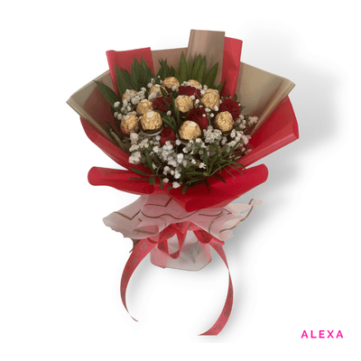 Alexa arrangement on a plain background: Ferrero Rocher chocolates with white fillers and greenery, wrapped in elegant red accents.
