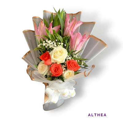 Althea arrangement on a plain background: Pink lilies and soft-toned roses with white fillers and greenery, wrapped in elegant gold accents.