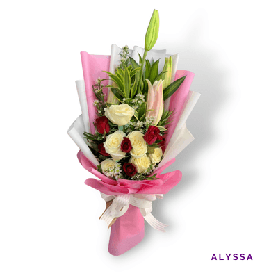 Alyssa arrangement on a plain background: Soft pink lilies and cream and red roses with delicate fillers and greenery, wrapped in elegant pink and white accents.