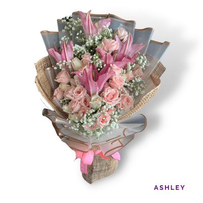 Ashley arrangement on a plain background: Romantic pink roses and stargazer lilies with baby’s breath, wrapped in elegant pink and neutral tones.