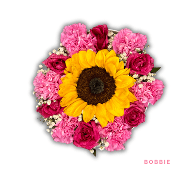 Bobbie: A radiant sunflower surrounded by pink roses and carnations, beautifully arranged in a sleek white hatbox.