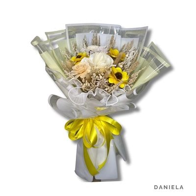 Daniela: Bright dried flower bouquet with cream and beige wood roses and a vibrant yellow wood sunflower, wrapped in soft yellow and finished with a satin ribbon.