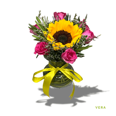 Vera: Six vibrant roses with a radiant sunflower centerpiece, beautifully arranged in glass, creating a cheerful, elegant display.